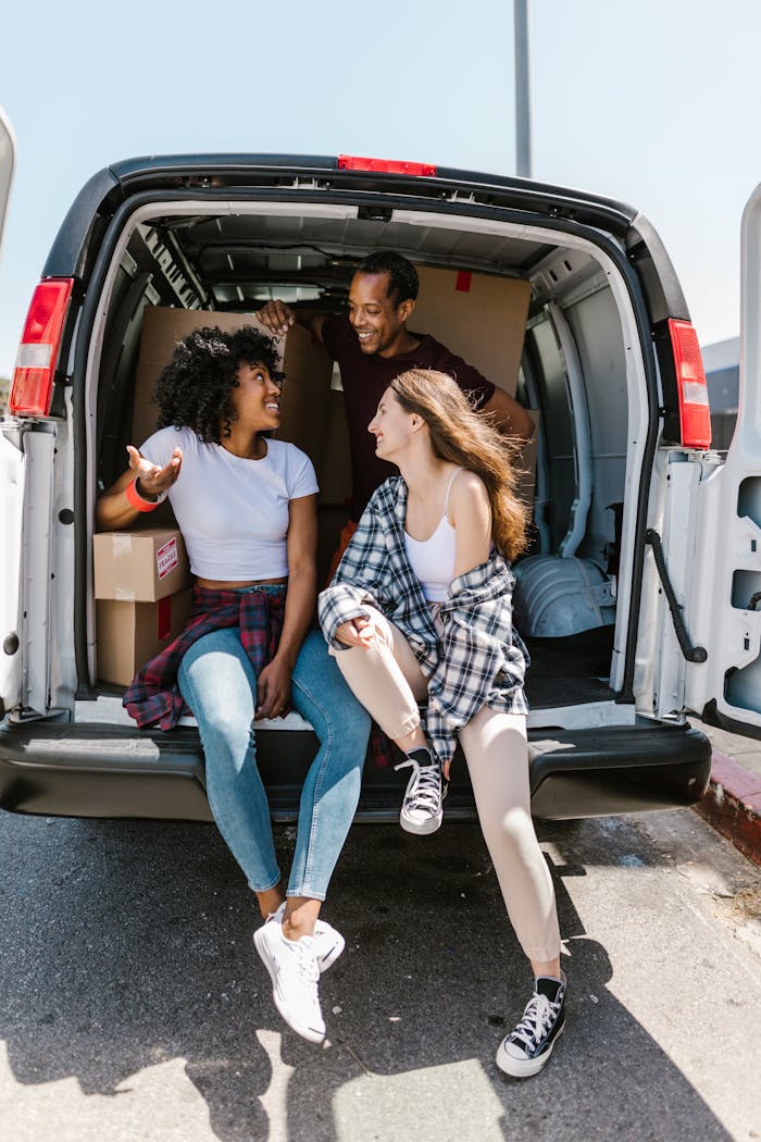 Three friends sitting on a van with moving boxes, enjoying the moving day experience.